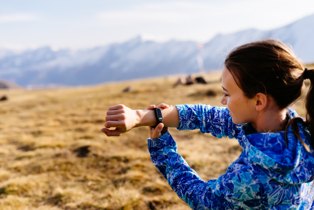 woman looks fitness bracelet background mountains